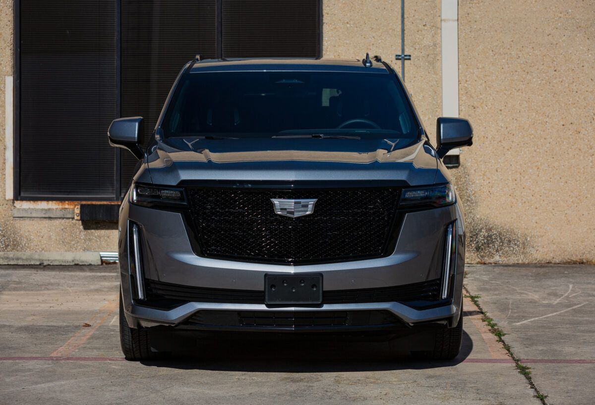 Gray Cadillac Escalade parked in front of a beige building, facing the camera.