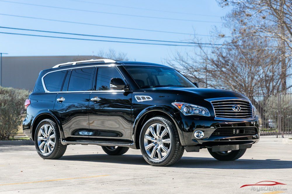 Black Infiniti QX80 SUV parked on a paved lot, sunny day. Chrome accents, silver wheels.