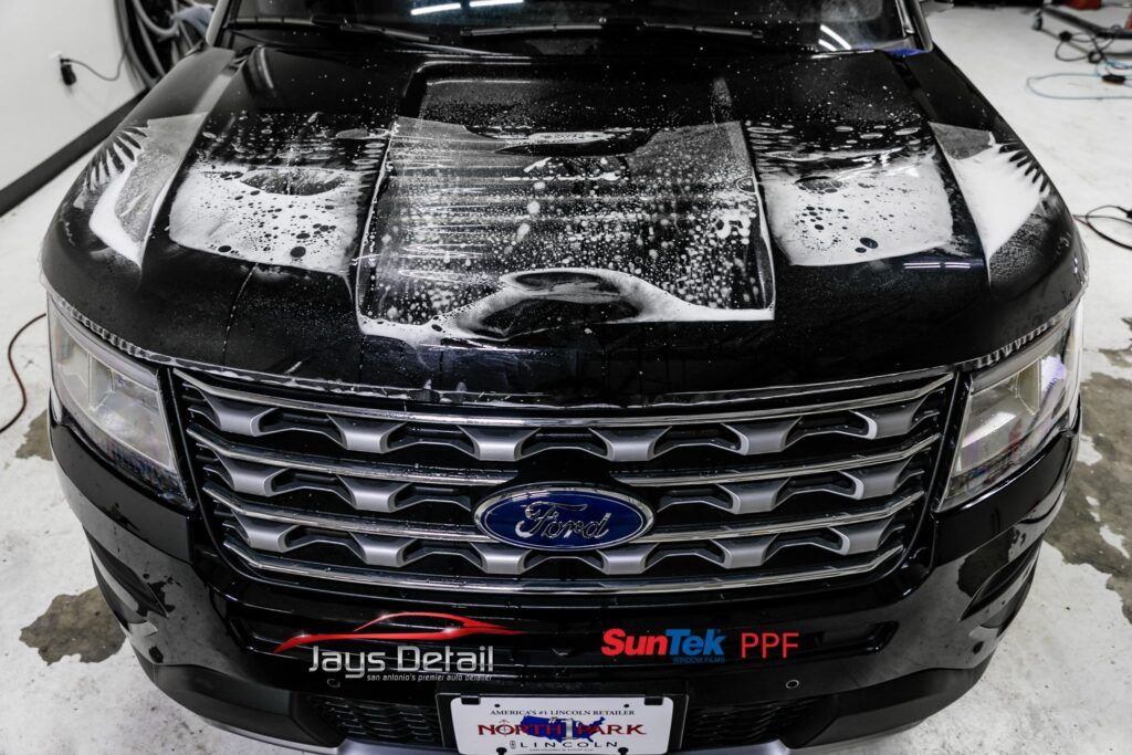 A black Ford SUV's hood with soapy water. Front view, license plate visible.