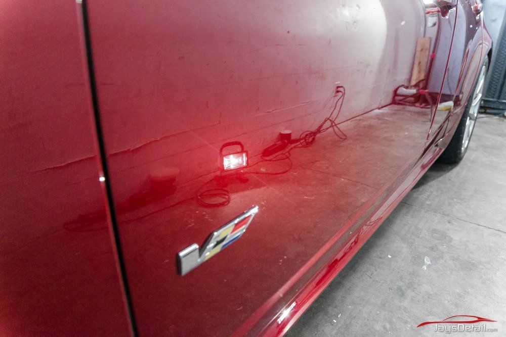 Red car door with V logo, reflecting a workshop setting with tools and light.