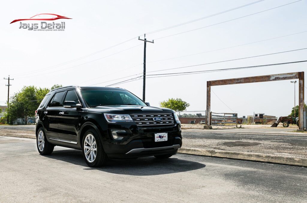 Black Ford Explorer SUV on a paved road under a bright sky, parked near a wooden structure.