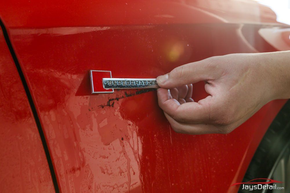 Hand removing car emblem from red vehicle.