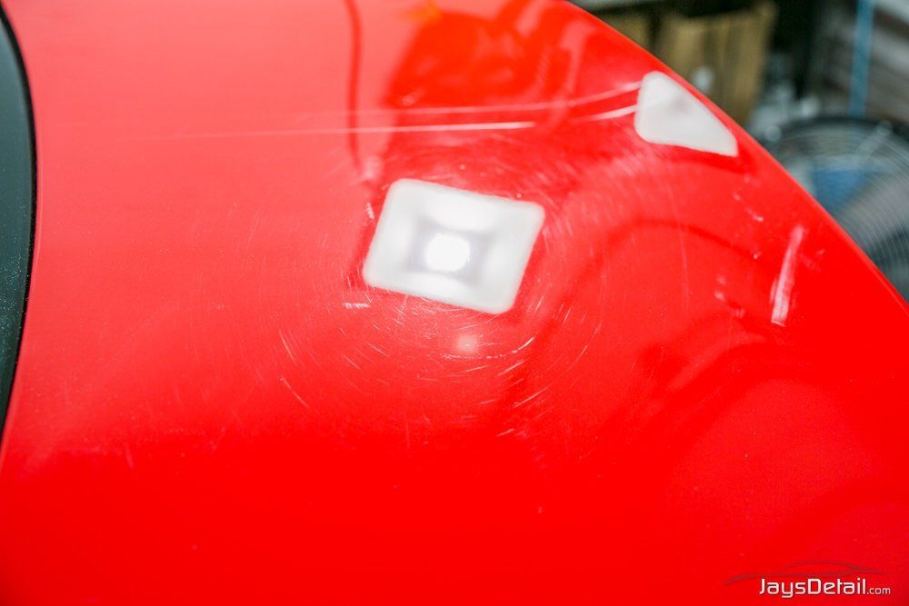 Red car surface with scratches and white squares, possibly for repair.
