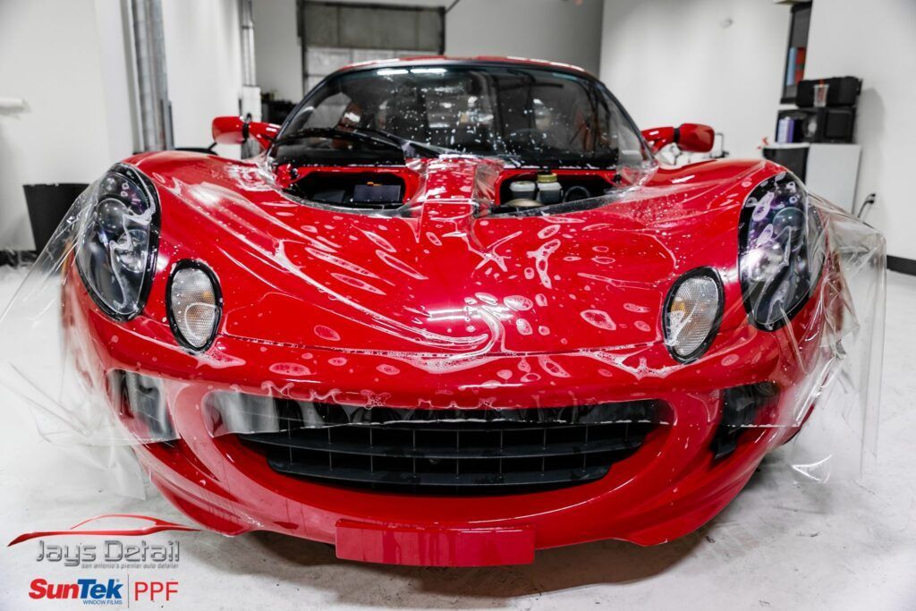 Red Lotus sports car wrapped in clear protective film, inside a garage.