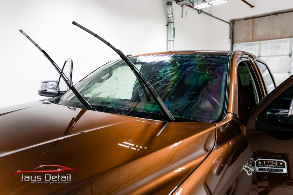 Brown truck being detailed; wet windshield with wipers up; indoors.