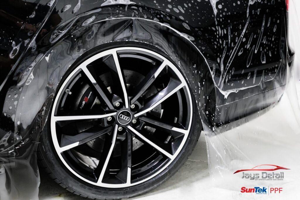 Black car wheel with white accents, being washed with soap.