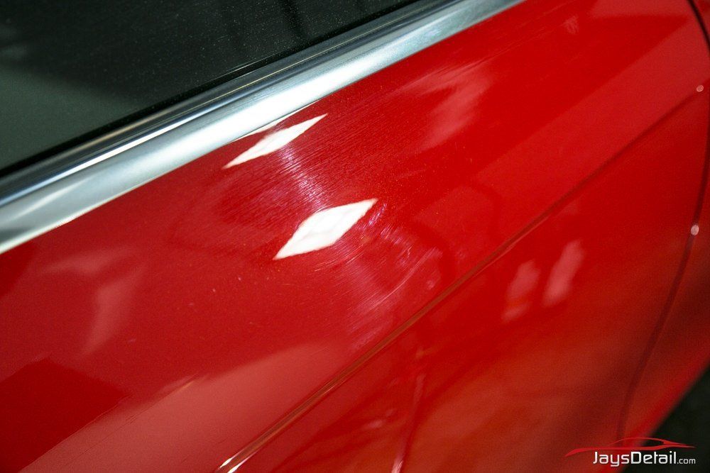 Red car door with scratches and reflections from a bright light.