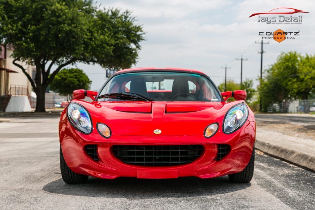 Red Lotus Elise sports car, front view, parked on a street.