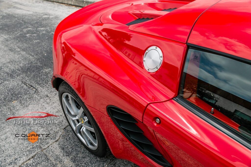Red sports car's rear, featuring fuel cap and wheel. Parked on a gray surface.