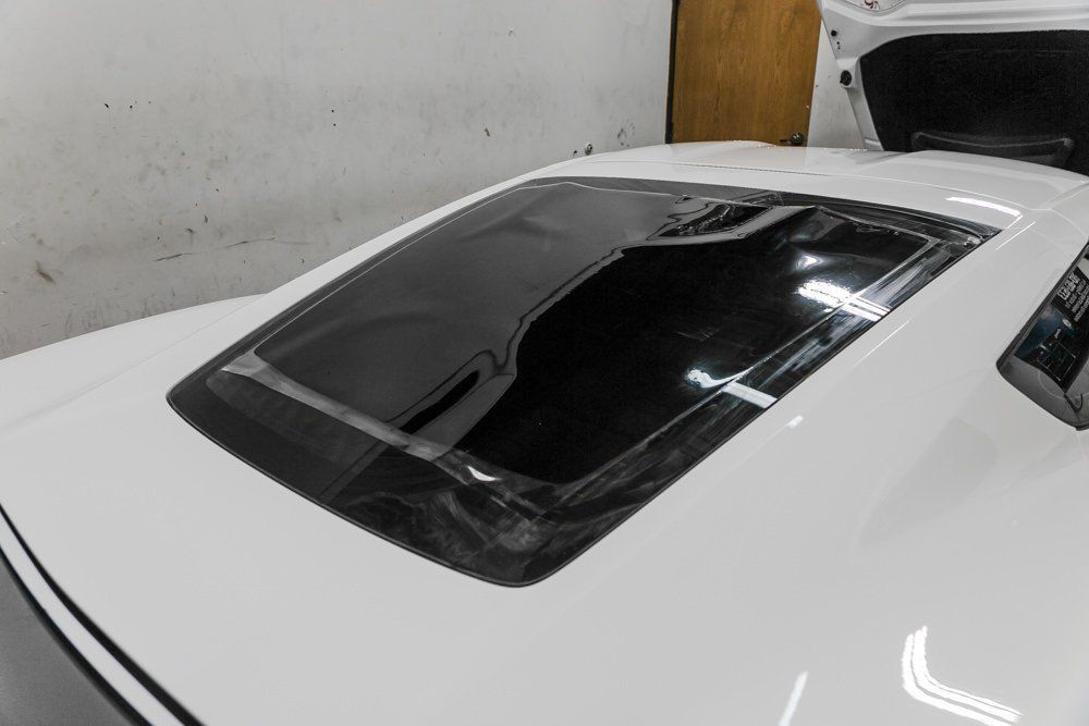 White car's rear with a cracked black back windshield. Trunk is open in a studio setting.