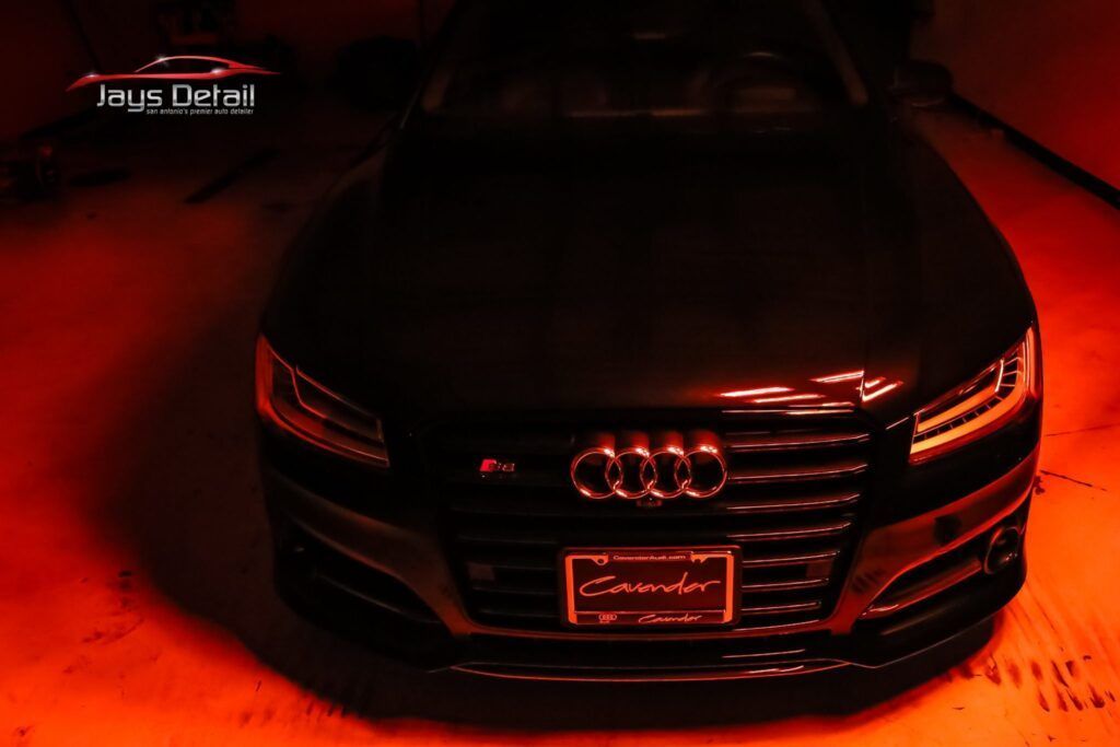 Front view of a dark Audi S8 sedan with red lighting highlighting its grille and front.