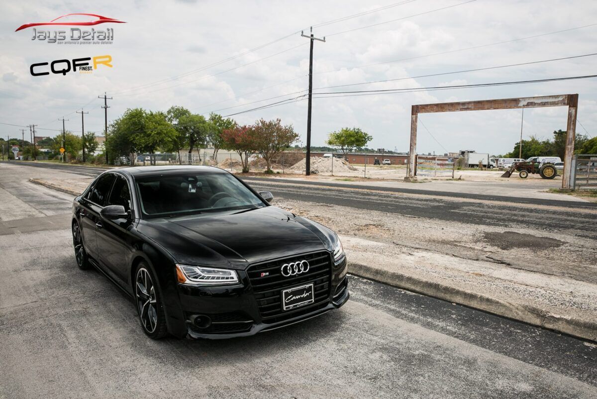 Black Audi S8 parked on a road with a rural background. Cloudy sky.