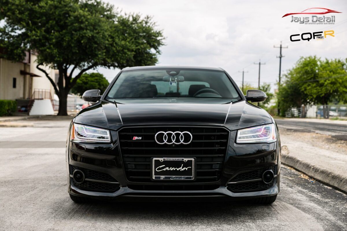 Black Audi S8 sedan parked on a street in front of a building with a tree in the background.