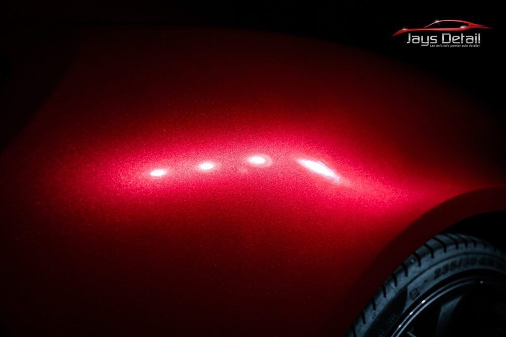 Red car fender illuminated showing paint imperfections, with tire visible.