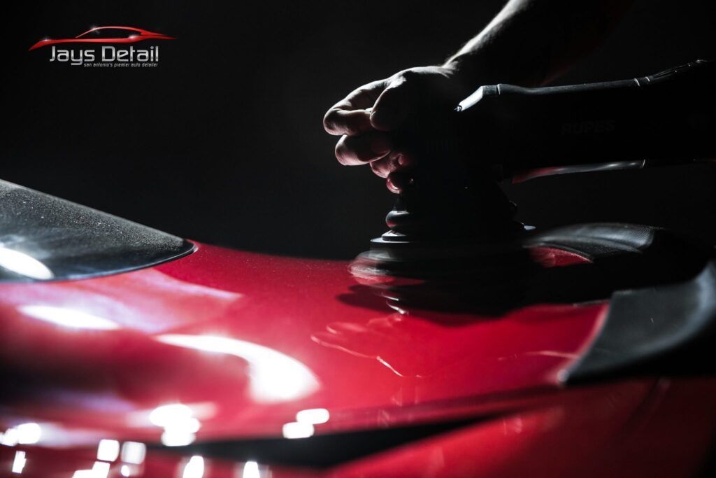 A person polishing a red car with a power tool in a dark setting, showcasing the detailing process.