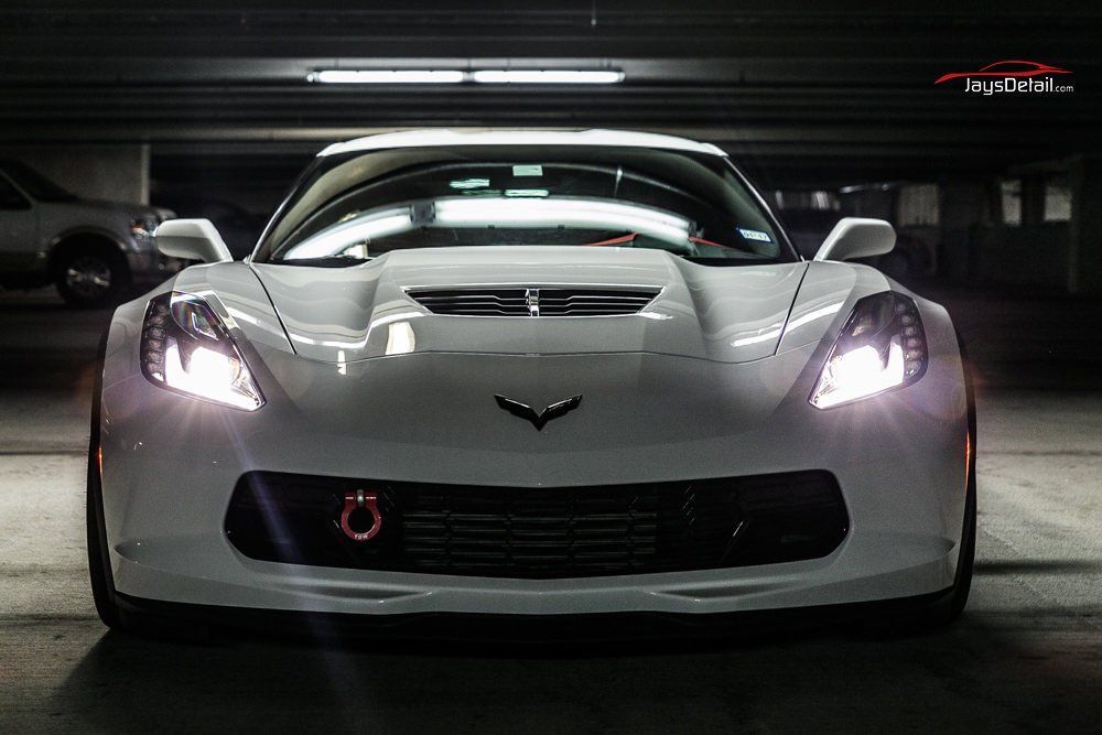 White Corvette with headlights on in a dimly lit parking garage.