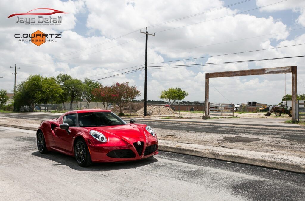 Red Alfa Romeo sports car on an asphalt road; sunny day with a cloudy sky.