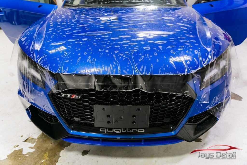 Blue car front with clear protective film applied; detail work in progress.