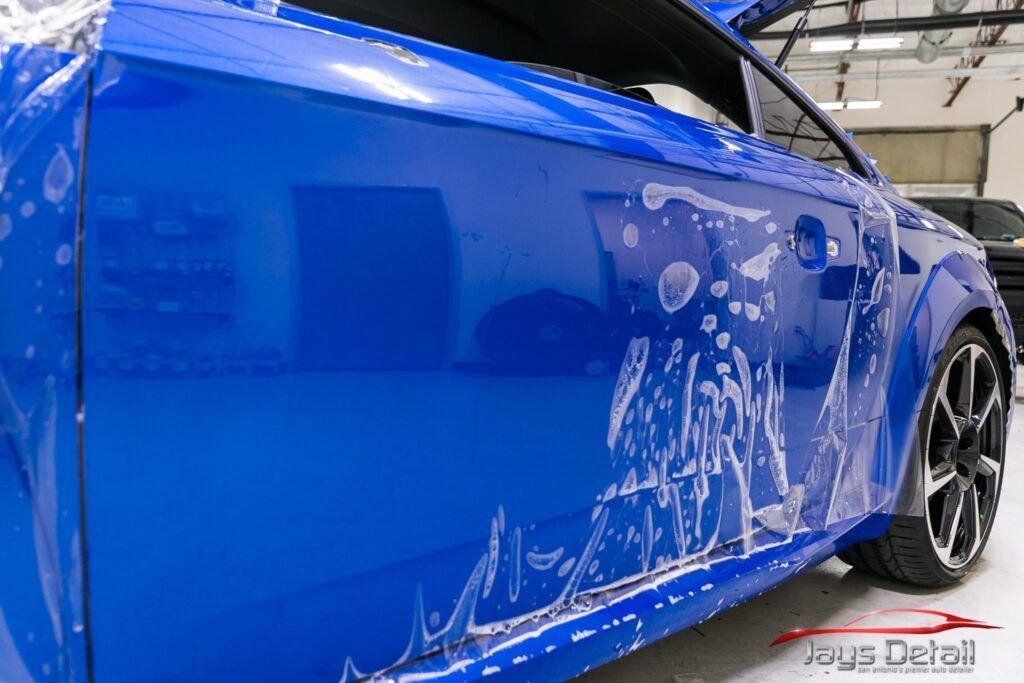 Blue car with protective film applied to its side in a workshop.