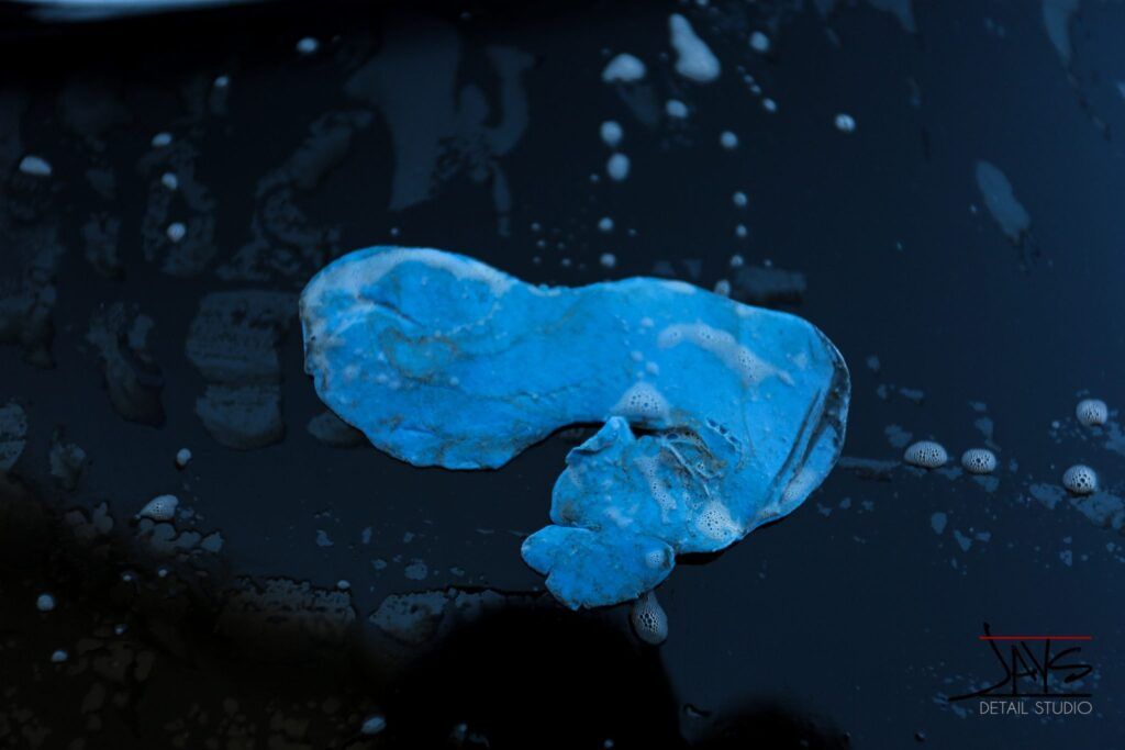 Blue-toned image. A blob-like form, possibly ice, on a reflective, dark surface with droplets.