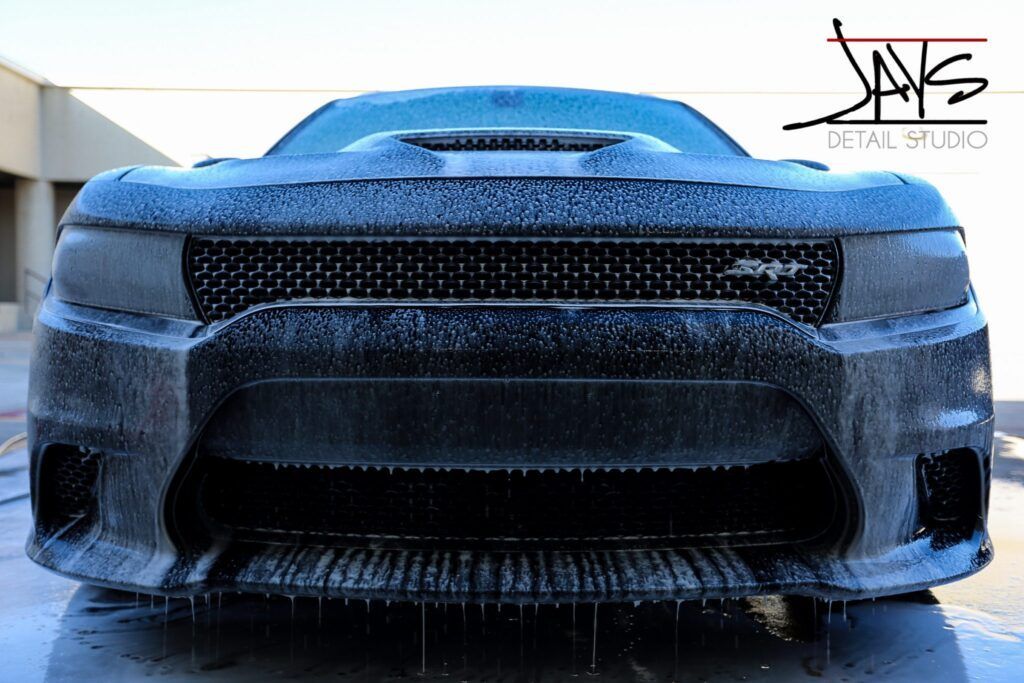 Black Dodge Charger being washed, front view, with water dripping down.