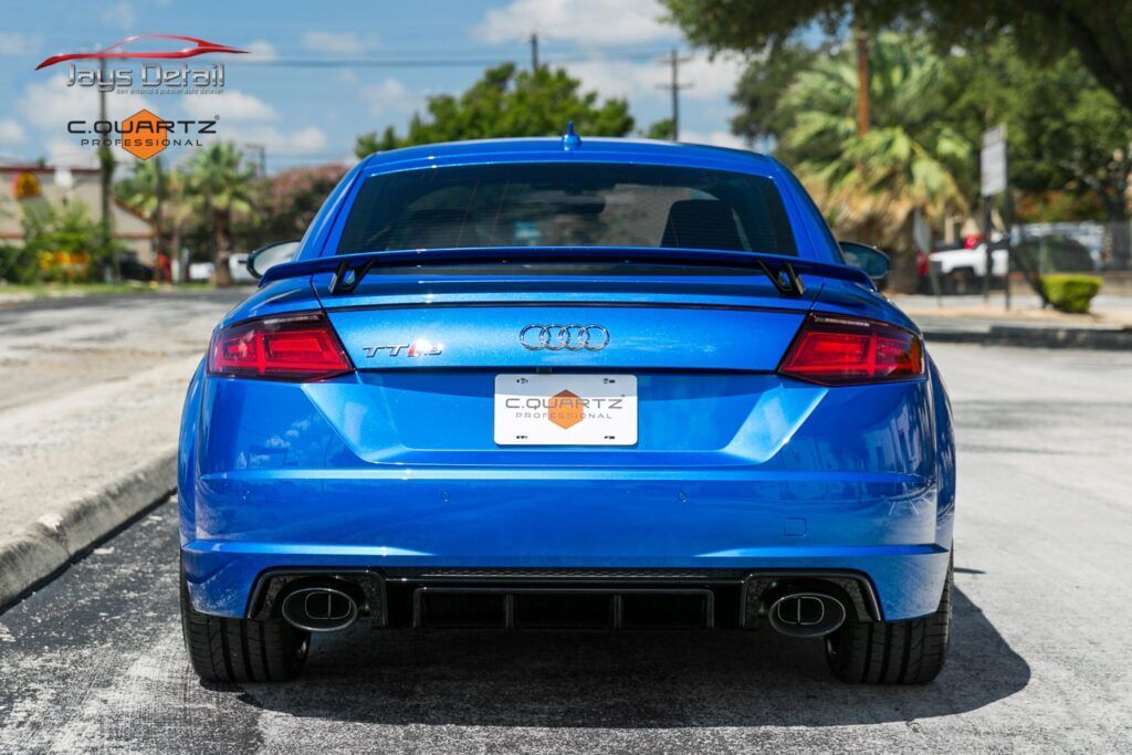 Blue Audi TT RS coupe, rear view, parked on a street.