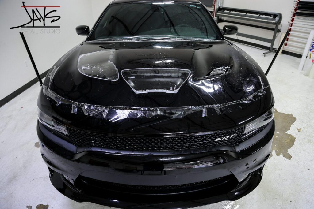 Black Dodge Charger with protective film being applied in a garage.