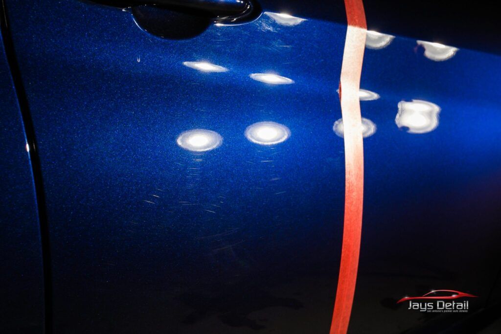 Blue car door with imperfections, partially polished, separated by a red tape line.