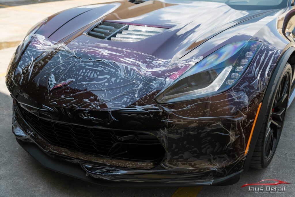 Dark-colored sports car with peeling protective film on the front.