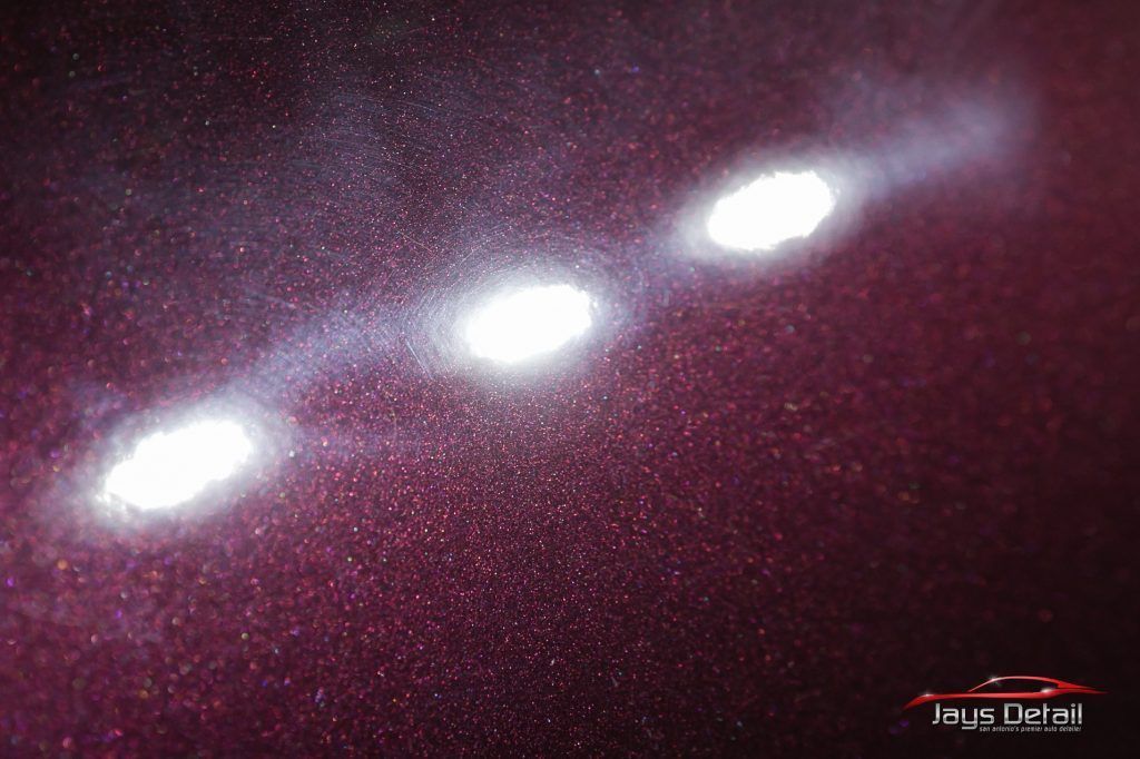 Three bright spots on a maroon car surface, likely highlighting paint imperfections or detailing.