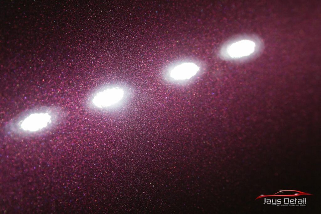 Close-up of a dark purple car paint with four bright circular reflections.