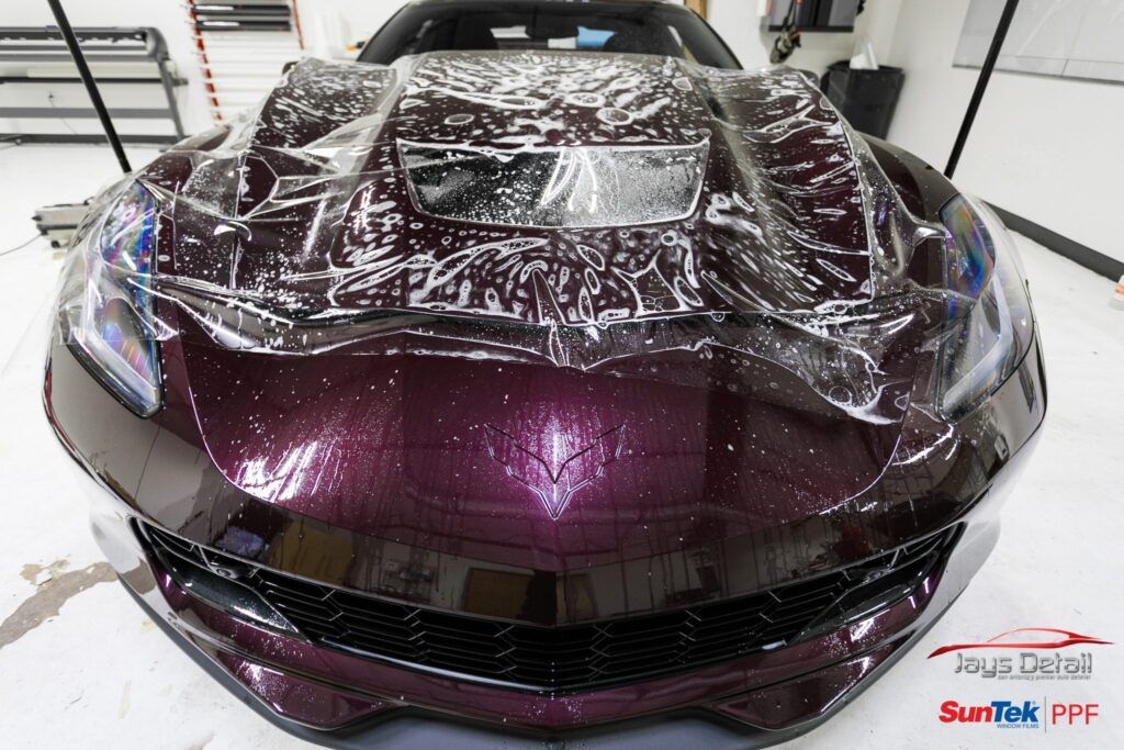 A deep purple sports car hood with protective film applied in a shop.