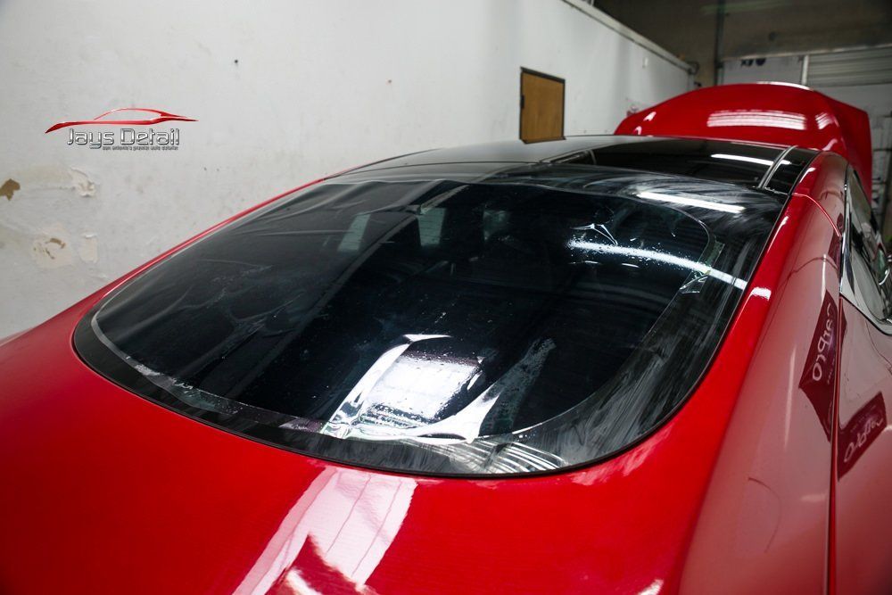 Red car with a black glass roof and open hood in a garage.