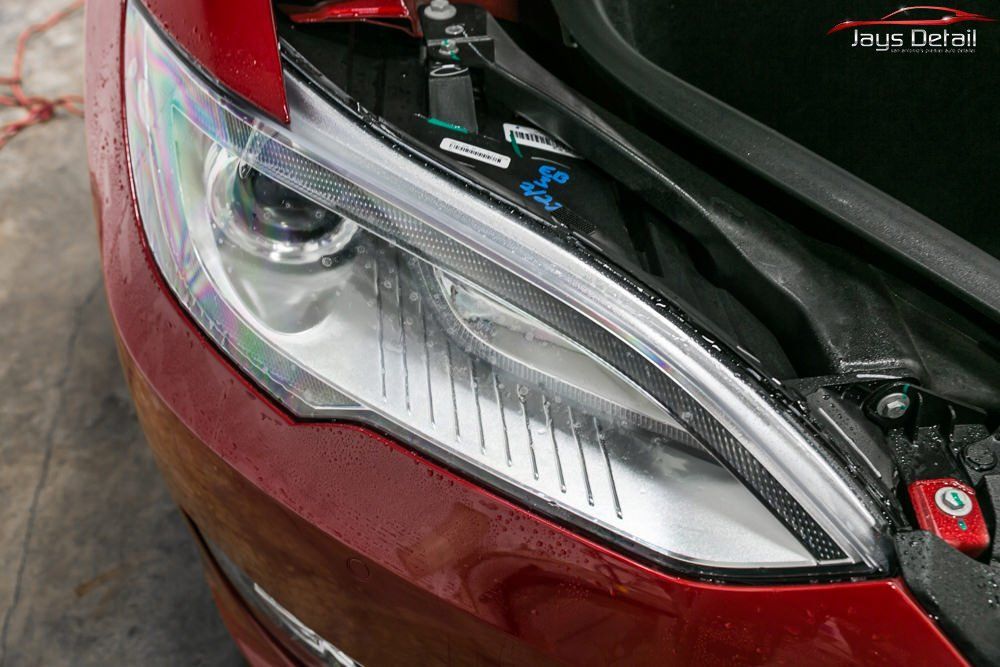 Close-up of a red car headlight, showing a clear, modern design with the hood open.