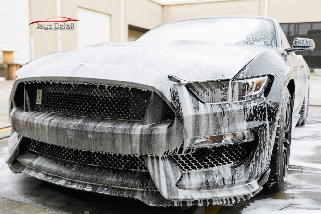 Black Ford Mustang covered in white foam during car wash.