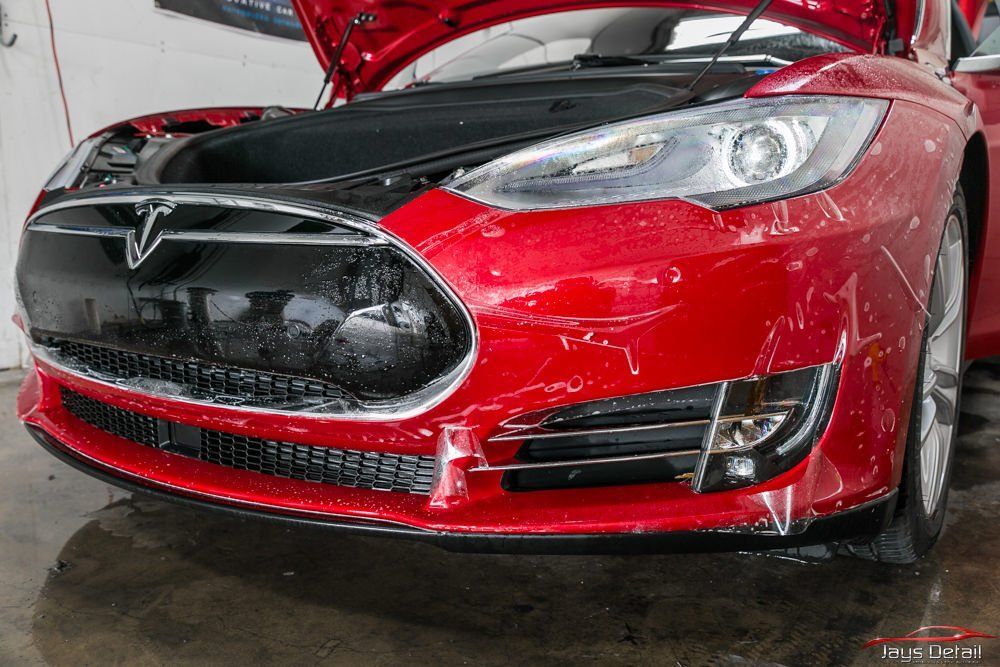 Red Tesla car being washed; hood open, close up of front, water droplets visible.