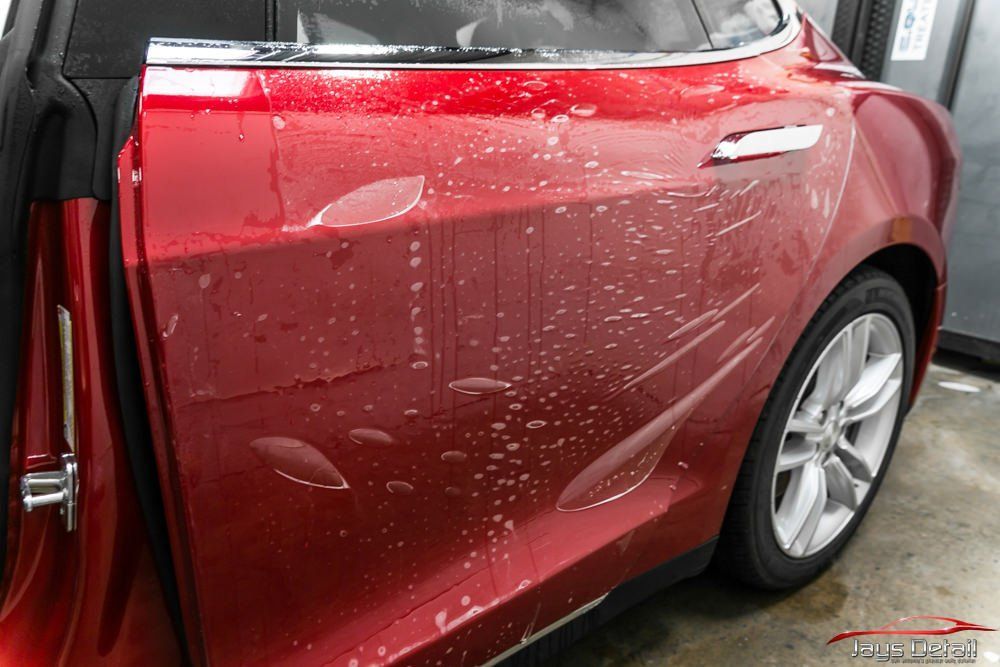 Red Tesla car door with clear protective film being applied.