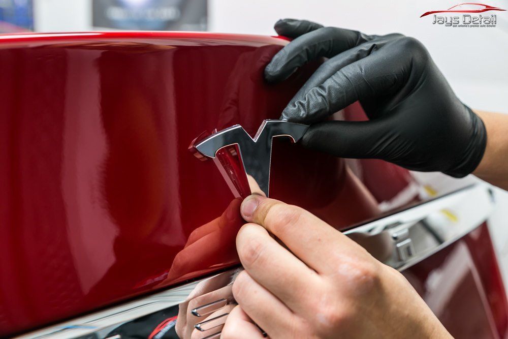 Person in black gloves attaching a chrome Tesla logo to a red car.