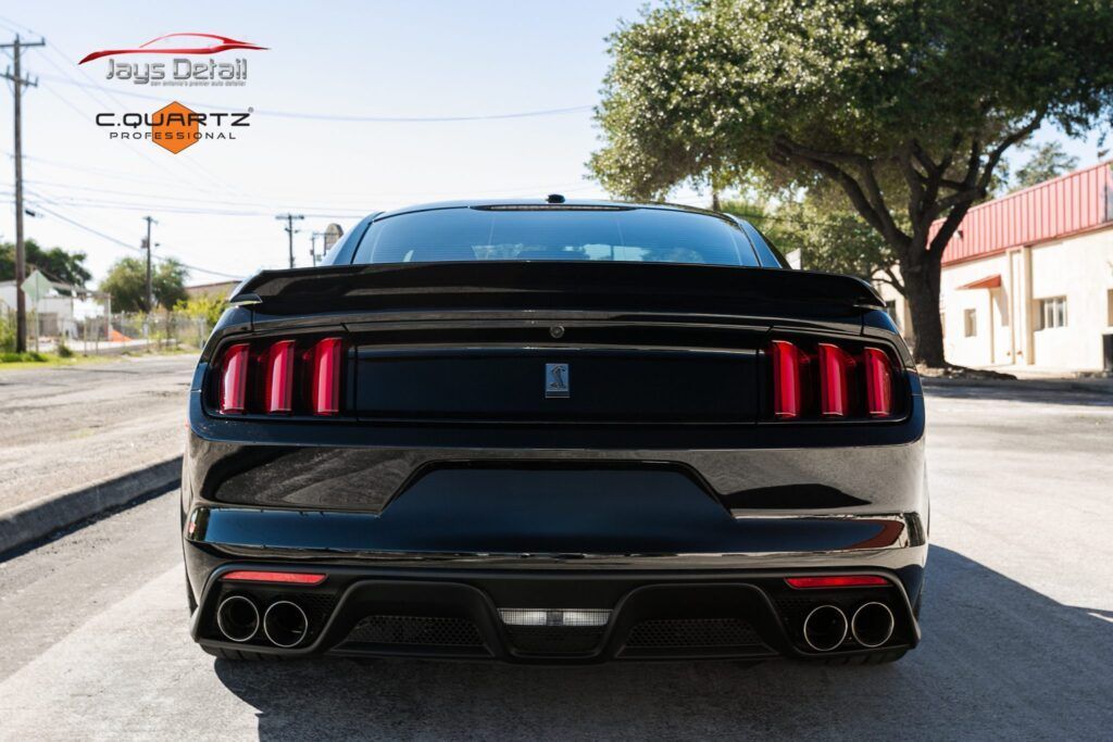 Black Ford Mustang rear view with red taillights, parked on a street.