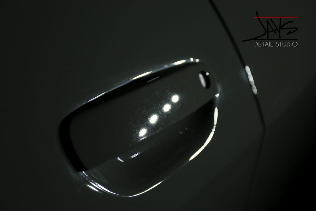 Car door handle reflecting lights, with a dark, glossy finish.