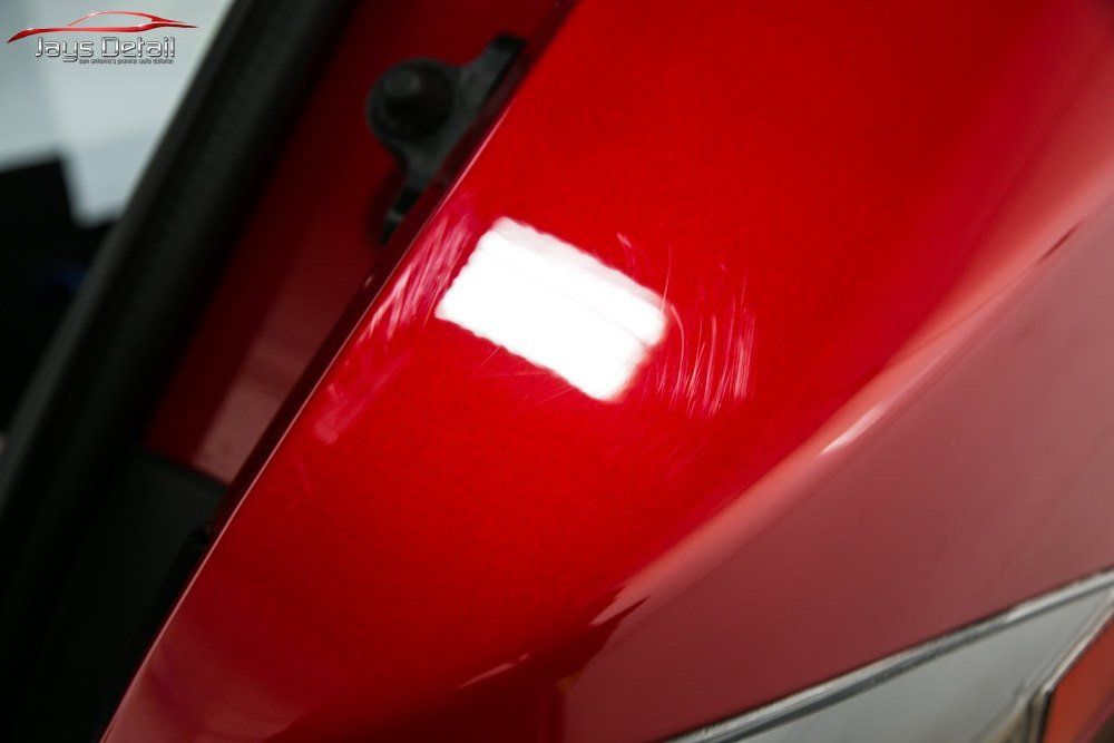 Red car fender with visible scratches reflecting bright light.