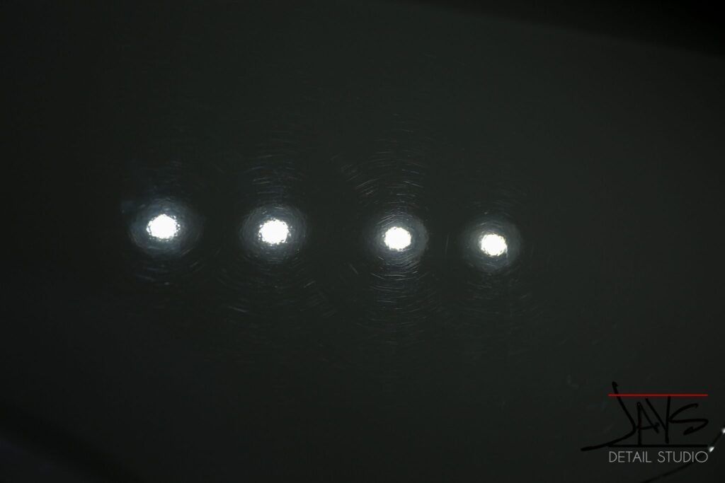 Four bright circular lights on a dark surface, possibly car paint, reflecting light.
