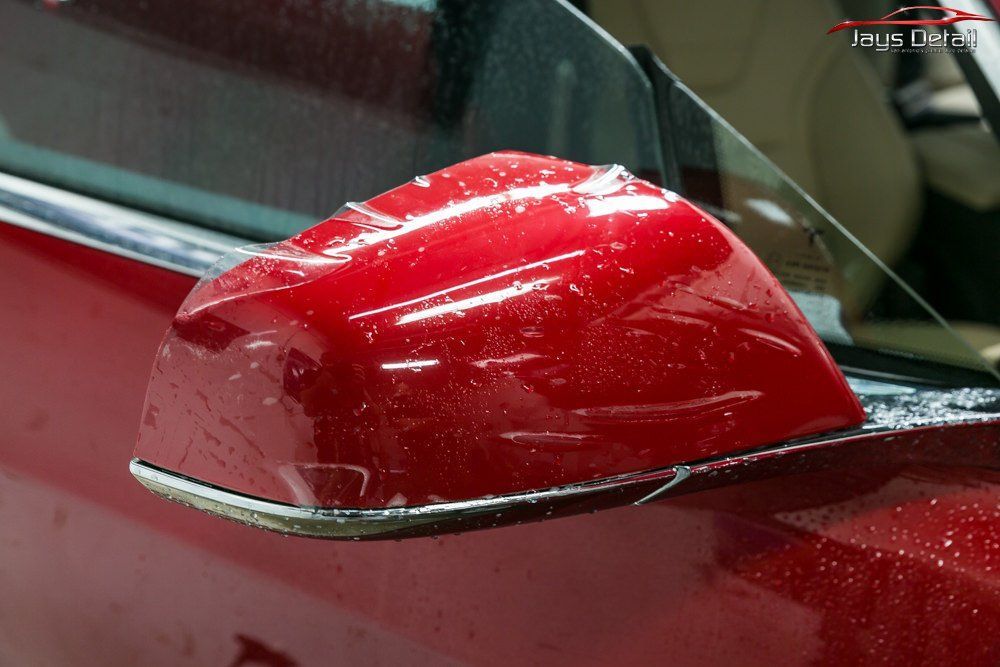 Red car side mirror, wet, close-up, showing chrome trim and the car's body.