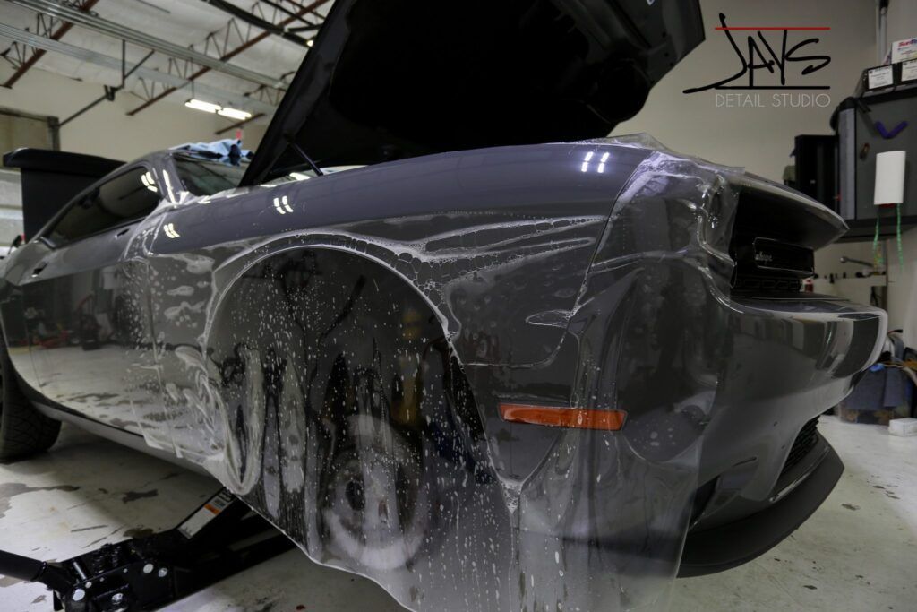Dark gray car with plastic film, being worked on in a shop.