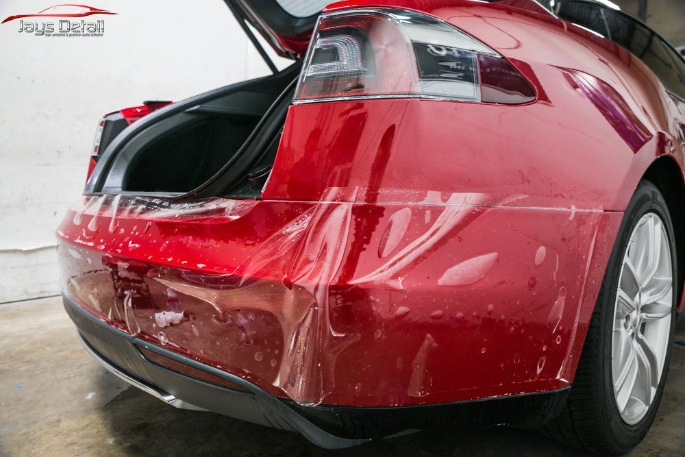 Red Tesla Model S with clear protective film being applied to rear bumper.