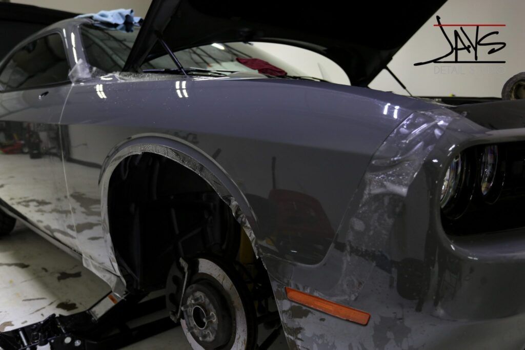 Gray Dodge Challenger with open hood, wheels removed, being worked on in a shop.