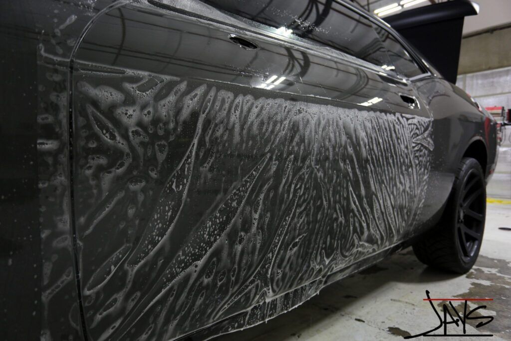 Black car with soapy water applied to the side, likely for detailing or cleaning.