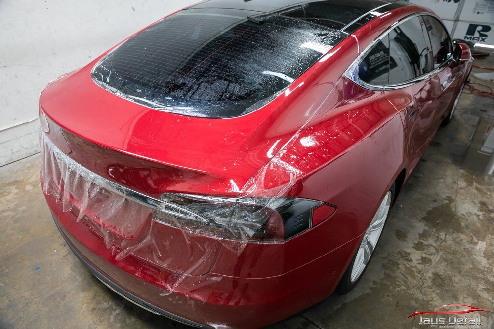 Red Tesla car with clear protective film being applied to the rear.