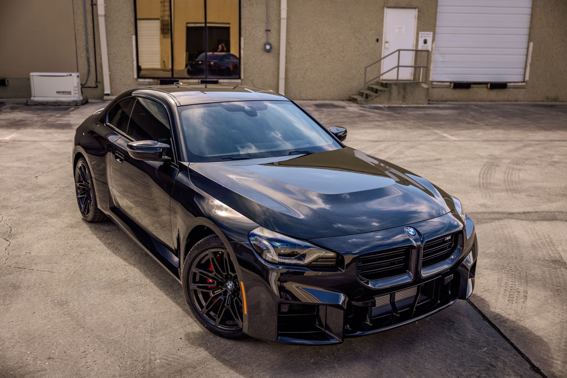 Black BMW M2 coupe parked outside a building, front view.