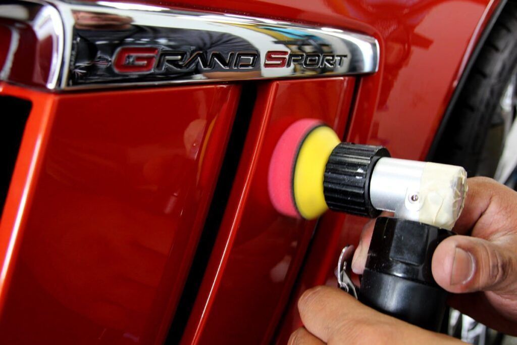 Person polishing red car panel with an electric polisher.